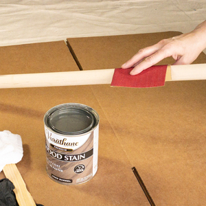 Using sandpaper on a dowel rod next to a can of Varathane wood stain.