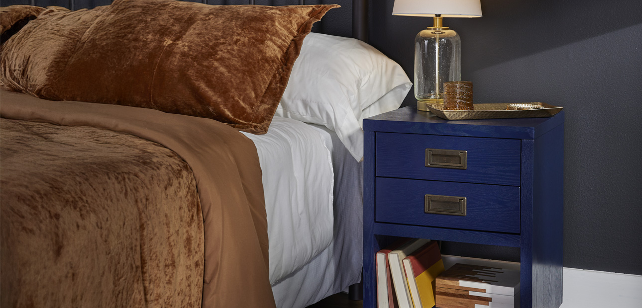 A blue nightstand with gold handles next to a bed.