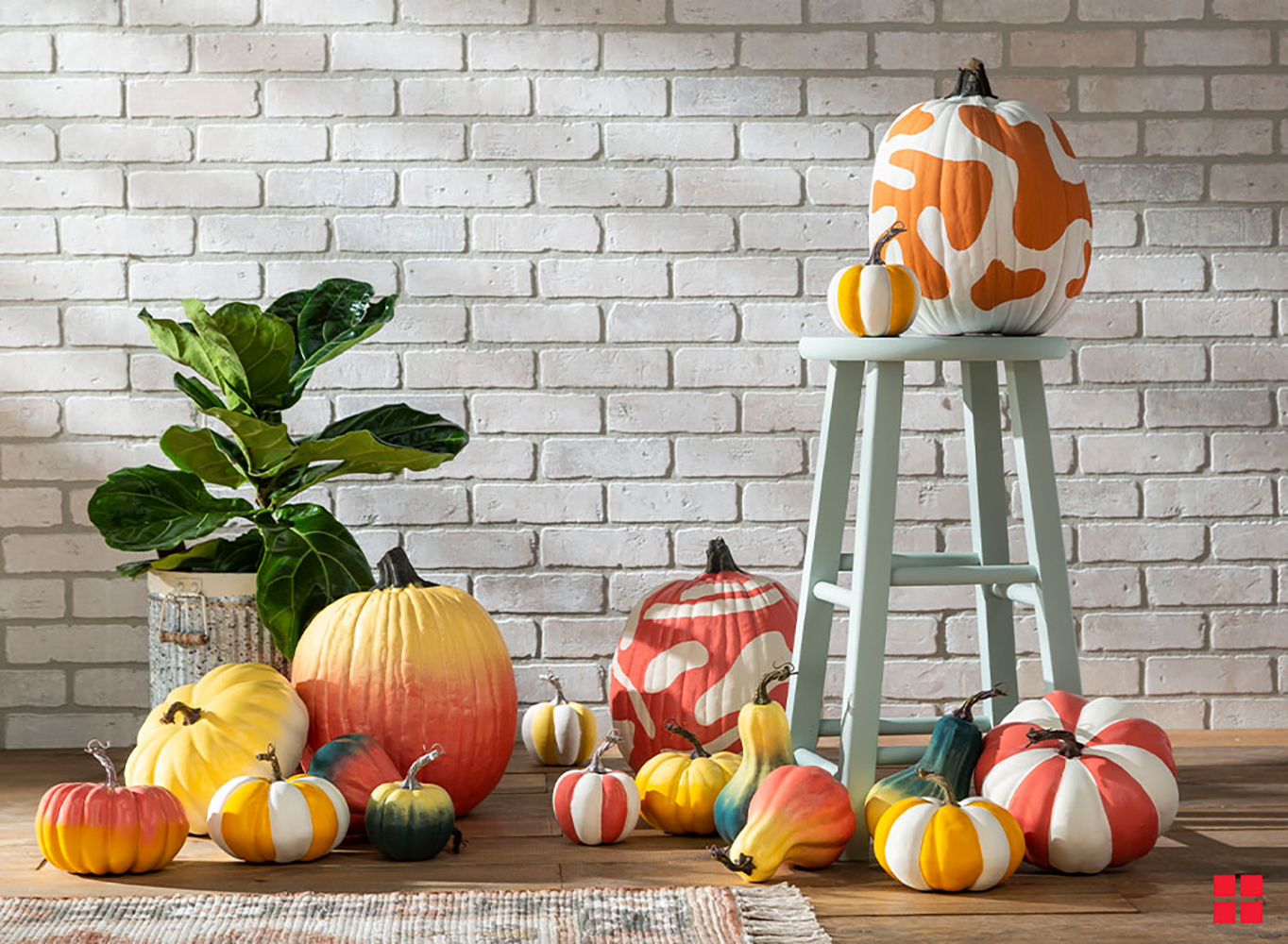 Pumpkins and gourds painted in different patterns on a porch with a stool. 