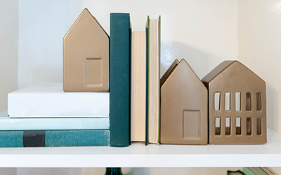 Three metallic gold bookends shaped like houses on a shelf with books. 