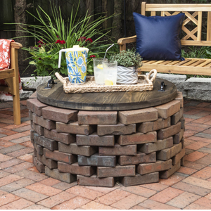 Clean patio with brick fire pit and stained wood fire pit cover with decorative tray and benches