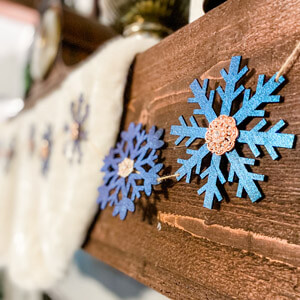 A string of decorative snowflakes in different shades of blue handing on a wooden mantle.