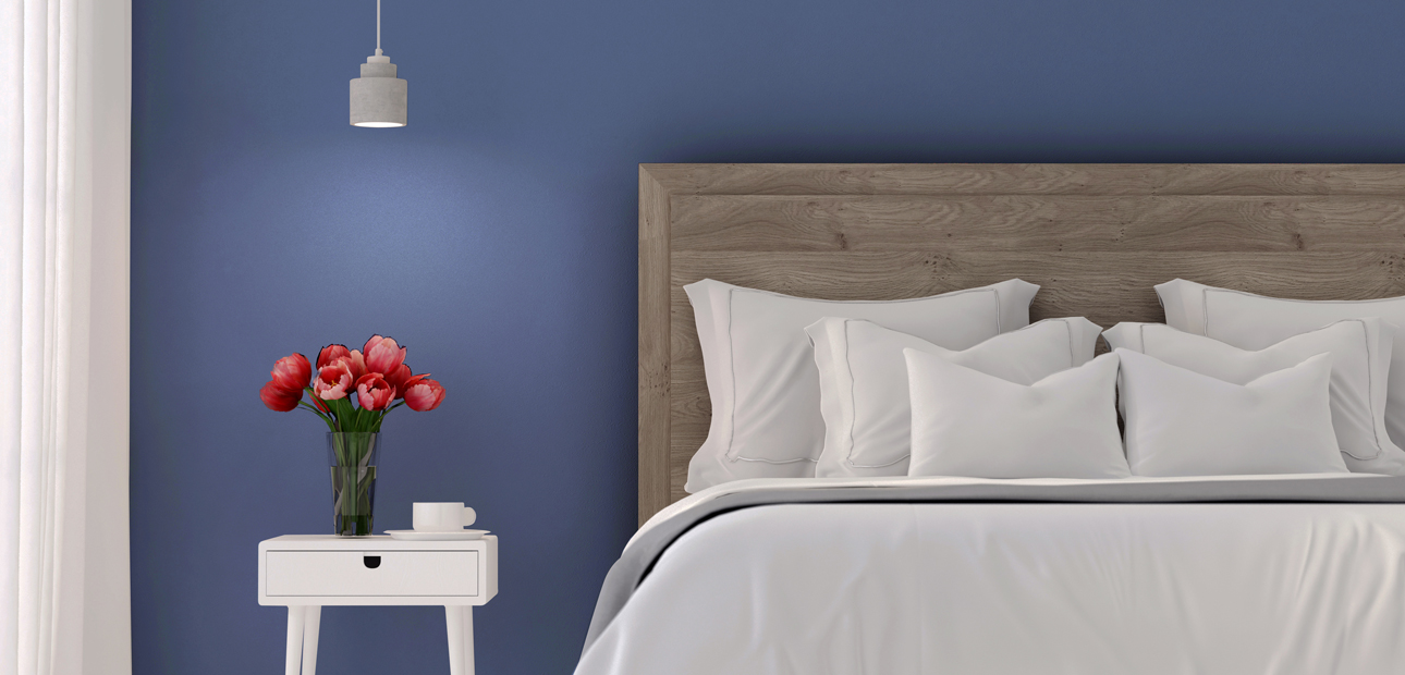 A blue wall behind a bed and white nightstand. 