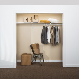 A chair, clothes and storage in a bedroom closet without doors. Room walls are white and inside closet is beige.