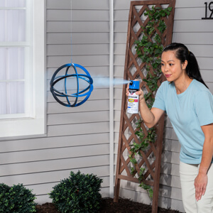 A woman applying blue spray paint to a metal orb. 