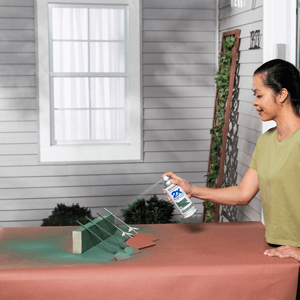 A woman applying green spray paint to the stems of decorative wooden flowers. 