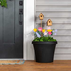 A black urn planter filled with green moss, colorful fake flowers and two wooden birdhouses. 