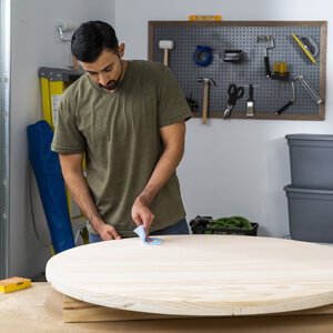 Man wiping sanding dust off wood round with tack cloth