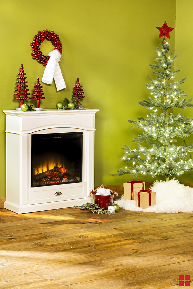A living room with a metallic red wreath and three metallic red decorative trees above a fireplace, and a Christmas tree in the corner.